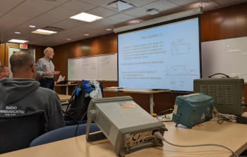 Measuring instruments sit on a table behind a class of students